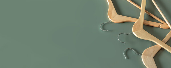 Naklejka premium Empty wooden clothes hangers on dark green background with copy space. Sale and shopping concept.