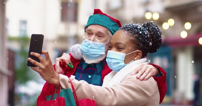 Happy african american woman in protective medical mask taking joint photo with man in santa costume. New Year's mood in quarantine.