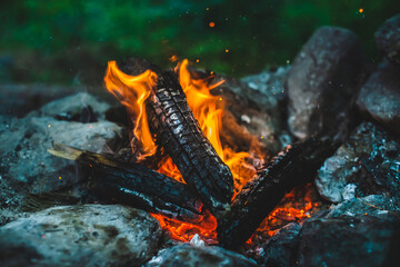 Vivid smoldered firewoods burned in fire close-up. Atmospheric background with orange flame of campfire. Full frame image of bonfire. Warm whirlwind of glowing embers and ashes in air. Sparks in bokeh