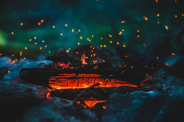 Vivid smoldered firewoods burned in fire closeup. Atmospheric background with orange flame of campfire. Wonderful full frame image of bonfire with glowing embers in air. Warm logs, bright sparks bokeh