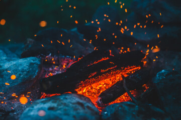 Fototapeta na wymiar Vivid smoldered firewoods burned in fire close-up. Atmospheric background with orange flame of campfire. Unimaginable full frame image of bonfire. Glowing embers in air. Warm logs, bright sparks bokeh