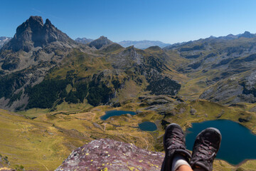 Out of focus boots of a hiker atop Ayous peak overlooking Ayous mountain lake and the Pyrenees mountains with Midi d'Ossau in front