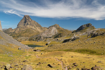 Mountain path with a lake and the Midi d'Ossau peak in the background surrounded by mountains, rocks and nature