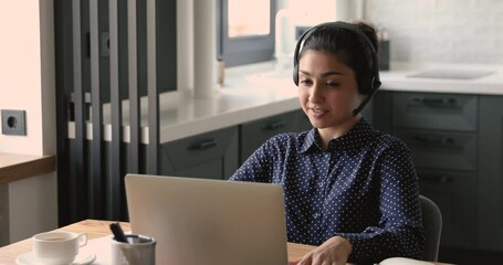 Happy young indian woman in headphones with mic holding online job interview with hr manager from home, sharing working experience, making self-presentation or discussing project with colleagues.
