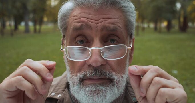 Grey-haired male looking at camera through eyeglasses, lens choice, cataract
