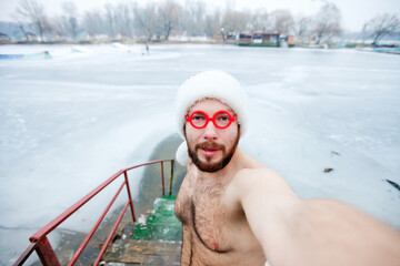A man, a walrus without clothes in a santa claus hat, takes a selfie in the winter near the ice...