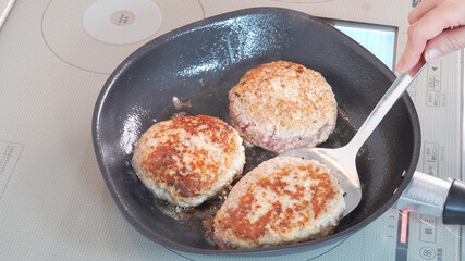 ハンバーグにフライパンで火を通す調理シーン