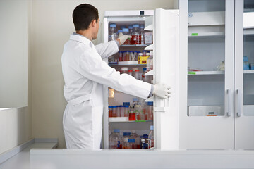 Scientist Taking Bottle From Refrigerator At Laboratory