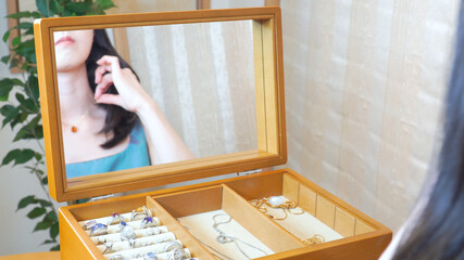 ネックレスを身につける鏡越しの女性の姿