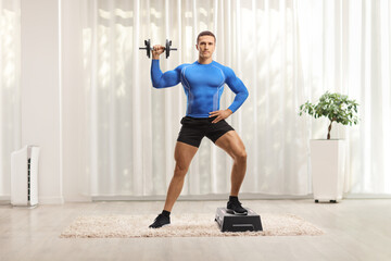 Fototapeta na wymiar Bodybuilder exercising aerobic on a stepper and holding weights at home