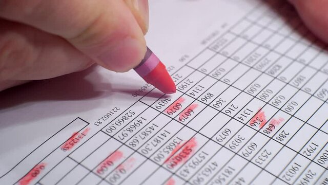 Hand makes notes with red marker on a piece of paper with financial information