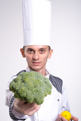 Male chef cook man in white uniform shirt posing isolated on white wall studio portrait. Cooking food concept. Mock up copy space. Broccoli and a lemon in the hands of the cook close-up on a white