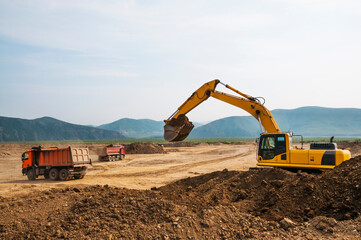  Earthworks on a summer day in a mountainous area. Excavators load soil into the tipper body