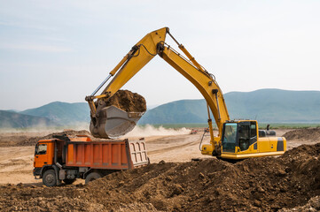  Earthworks on a summer day in a mountainous area. Excavators load soil into the tipper body