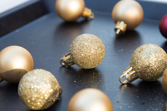 Small golden sparkling Christmas balls on black tray. New year decorations. Close up of Xmas toys. Holiday menu. Wallpaper and postcard picture. Decorations for pine tree. Social distance. Shiny