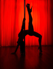 Dark silhouette of a slender sexy pole dancer on a red background