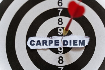 A piece of paper with the text is nailed to the target with a dart - CARPE DIEM