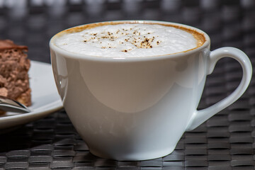 Cup of cappuccino with a slice of cake on the background
