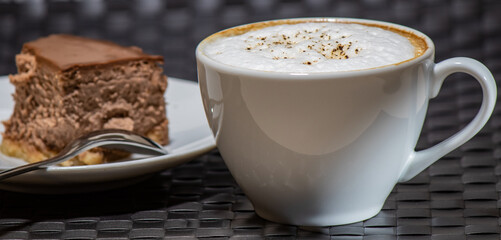 Cup of cappuccino with a slice of cake on the background