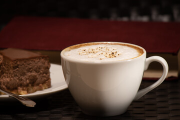 Cup of cappuccino with a slice of cake on the background of the book