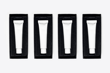 Close-up of empty cosmetic tube bottles, packaging in black box on white background.