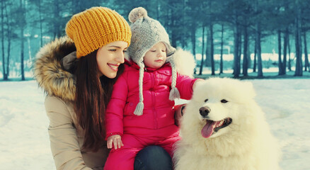 Portrait of happy mother and child with white Samoyed dog in winter park