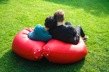 two Young brunette girl  sitting in 2 bean bag chairs in the park and looking each other with...