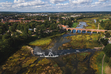 aerial drone shot view look from above of a waterfall in Kuldiga Latvia longest widest in Europe Venta river sunshine sunlight day green old bridge over 