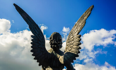 Sculpture of a wing angel on blue sky background. back view.
