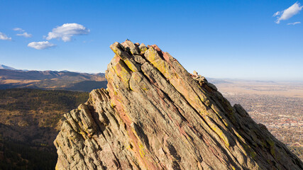 Drone photo of a flatiron in Boulder, Colorado. This aerial view shows the rock face coming above the horizon with a blue sky and a city in the background