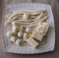 Top view shot of different cheese on white Porcelain plate. Lots of white cheese on the table and sliced.