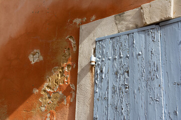 A red facade of a Provencal house. White borders around the windows. Light blue shutters.
