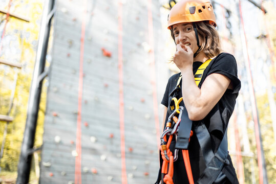 Portrait Of A Well Equipped Young Woman Feeling Scared Before Climbing The Wall At Amusement Park. Woman Is Afraid Of Heights