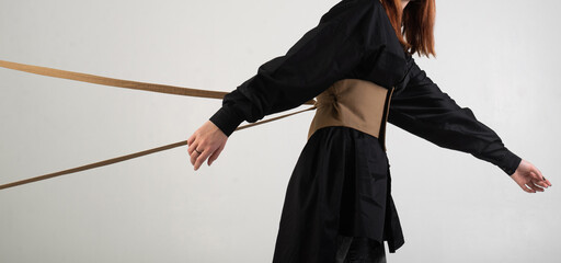 girl in black, held from behind with ropes on a white background, unrecognizable