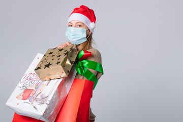 Lady in a medical mask and Santa hat with big gift bags on a white background. Pandemic, shopping and holidays concept.