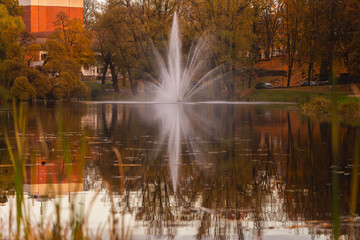 fountain in the city park in autumn fall in the lake pond reflection mirrored image