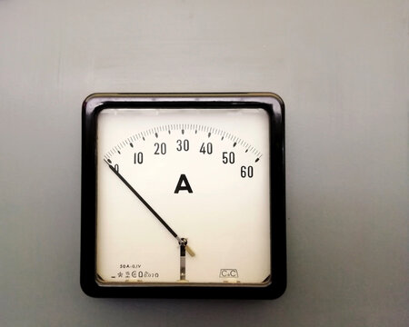 a large square industrial ammeter with an analogue dial with numbers with standard electrical symbols on a white dial on a grey background - Powered by Adobe