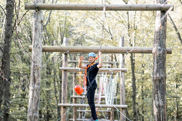 Well-equipped man having an active recreation, climbing in a rope park with obstacles in the forest