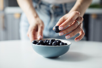 Woman's hands take blueberries from the plate. On the background of a beautiful kitchen.