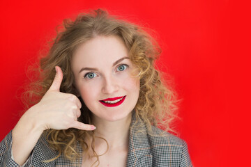 Young surprise woman with curly hair over red wall making phone gesture. Call me back sign. Communication symbols.