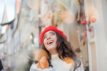 Christmas. Portrait of a young beautiful woman in a red beret in a European city. Young woman holds a paper bag with baguettes. 
