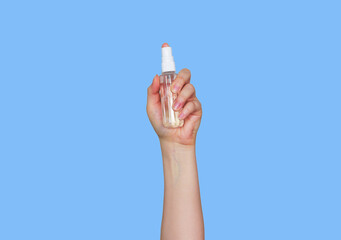 Female hand holding spray cream bottle of lotion isolated. Girl give cosmetic products on blue background