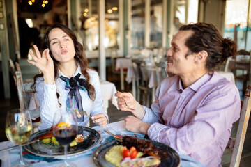 Beautiful and happy young married couple having a great time eating dinner in a rustic restaurant, talking and enjoying