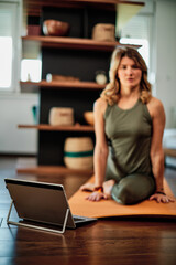 A middle-aged woman doing yoga, following an online tutorial on laptop during corona virus pandemic.