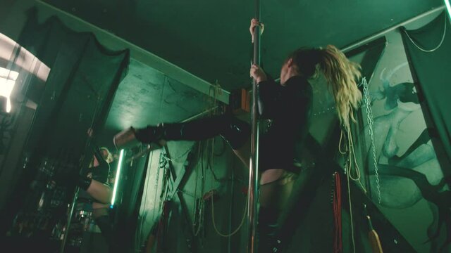 Sexy young stripper in latex suit pole dancing in bdsm room
