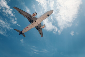 White commercial huge plane is flying above clouds in the blue sky, view from below