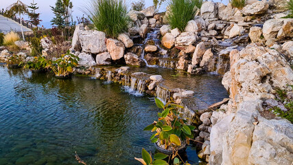 Layered rocky waterfall in large pond with plants