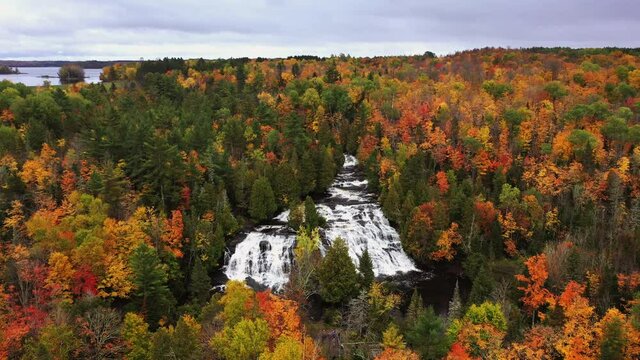 Beautiful push in travel aerial flying towards Bond Falls waterfall on the Middle Branch Ontonagon River surrounded by evergreen and deciduous trees with autumn colored foliage in Upper Michigan.
