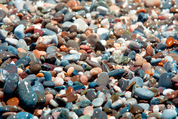 A lot of  beautiful little wet stones on the beach. Colored sea pebbles glisten in sea water. sea foam