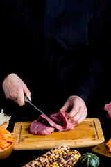 hands of the chef cut meat on the black table